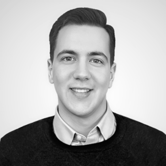 A professional headshot of a man smiling, wearing a collared shirt and dark sweater.